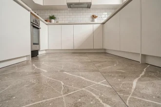 Carrelage en grès cérame grand format dans une cuisine moderne aux tons greige avec meubles blancs mats et plan de travail en quartz
